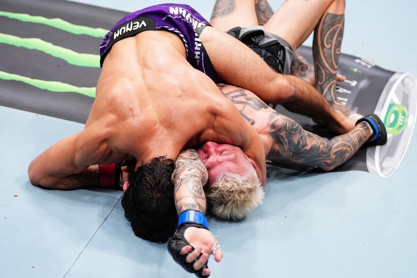 A fighter finishing an arm triangle, the man underneath trapped and turning red.