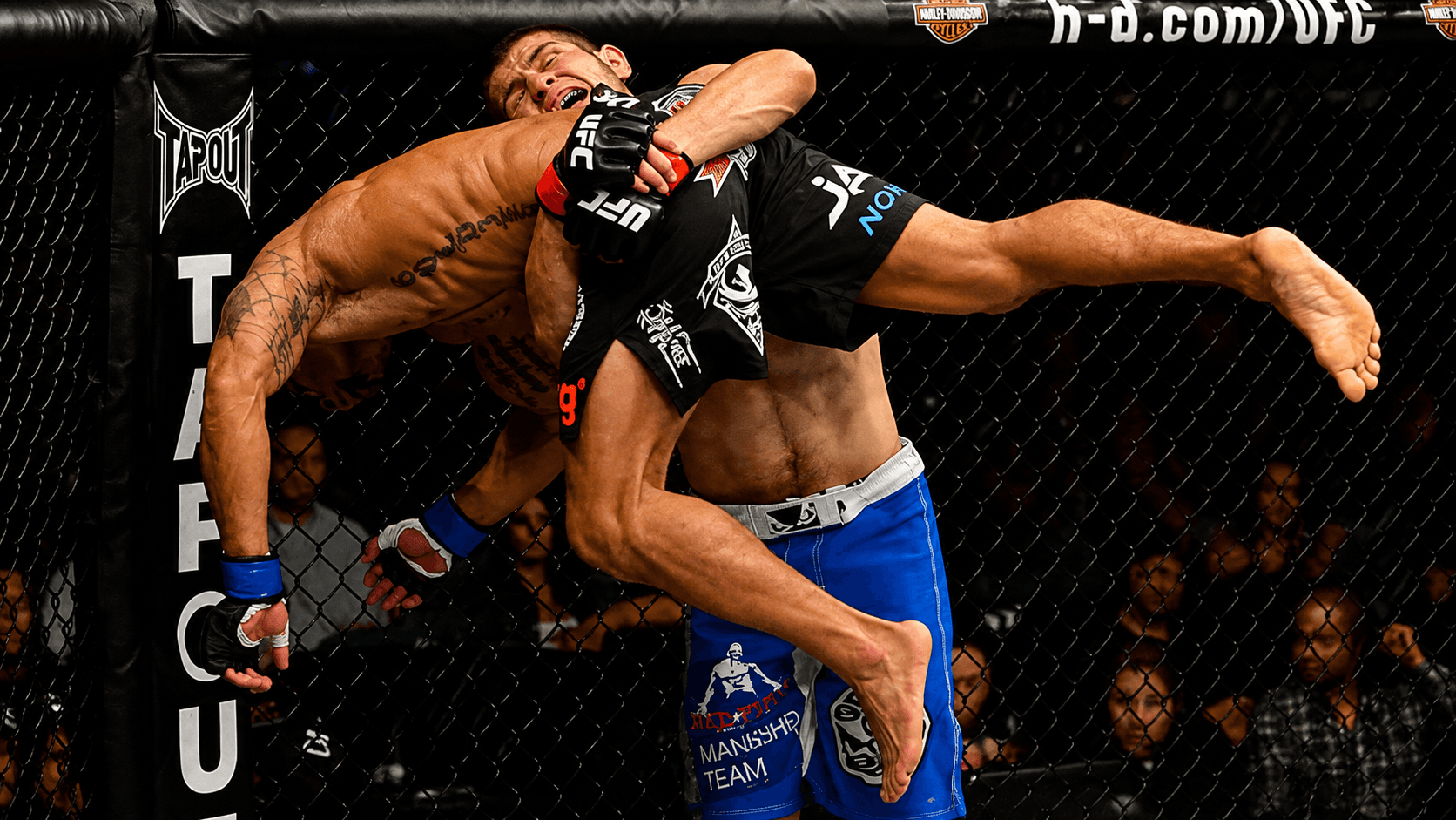 A fighter driving through a double-leg takedown in the centre of the cage.