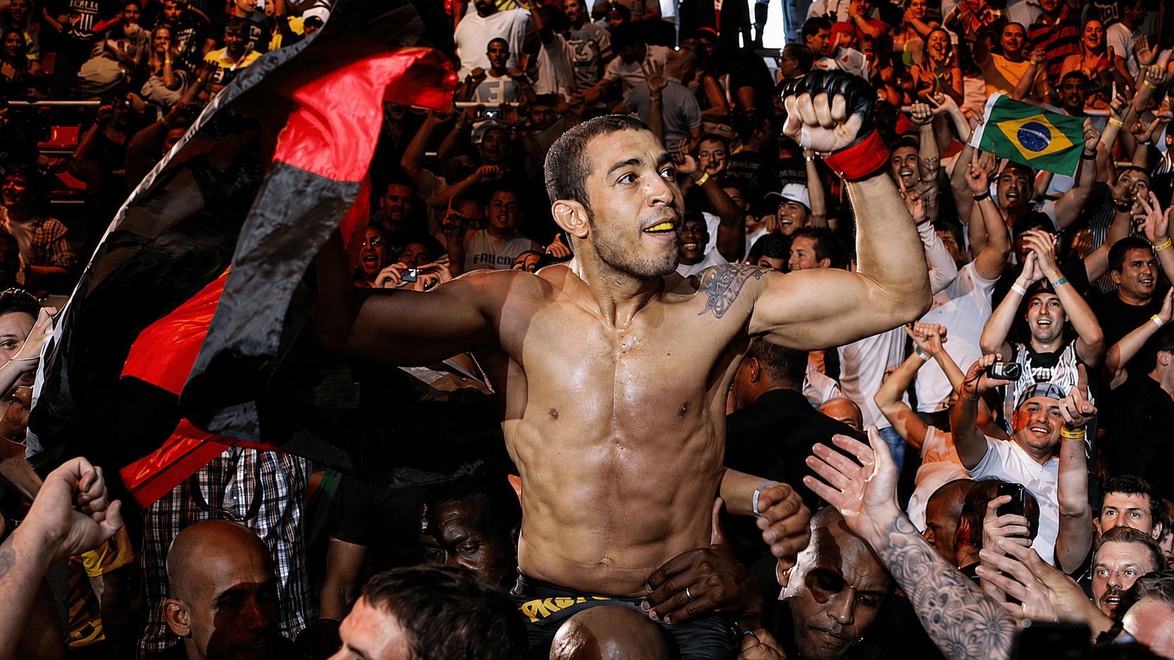 A fighter carried shoulder-high into a packed crowd, a Brazilian flag raised behind him.