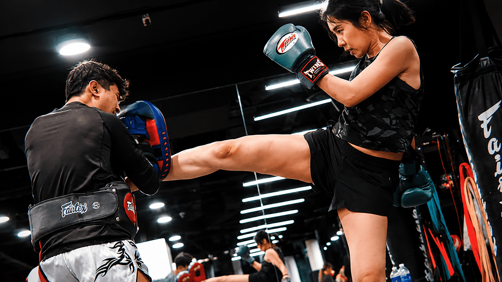 A fighter driving a kick into a coach's pads in the gym.
