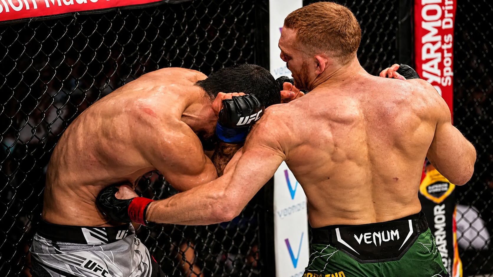 Two fighters trading at close range against the cage, one man's punch stopped dead on the other's glove.