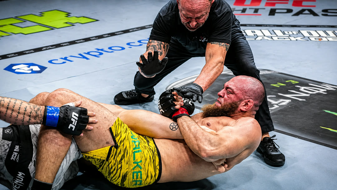 Valter Walker holding a leg submission on the mat as the referee steps in.